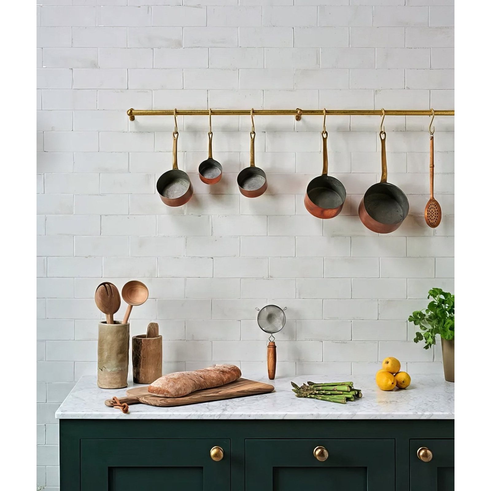 A set of five copper pots with brass handles hanging from a gold-colored rod in pottery porcelain natural cotton brick style