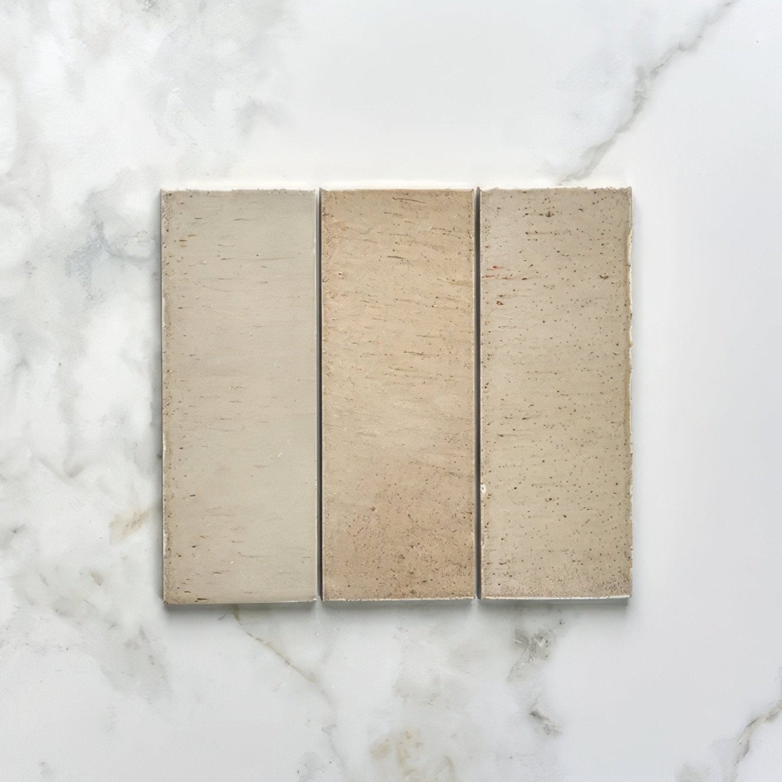 Three rectangular beige oatmeal porcelain bricks with subtle texture and natural tone variations on marble surface
