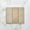 Three rectangular beige oatmeal porcelain bricks with subtle texture and natural tone variations on marble surface