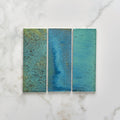 Three rectangular pottery porcelain ocean blue brick tiles with textured glazed surfaces in shades of teal and blue