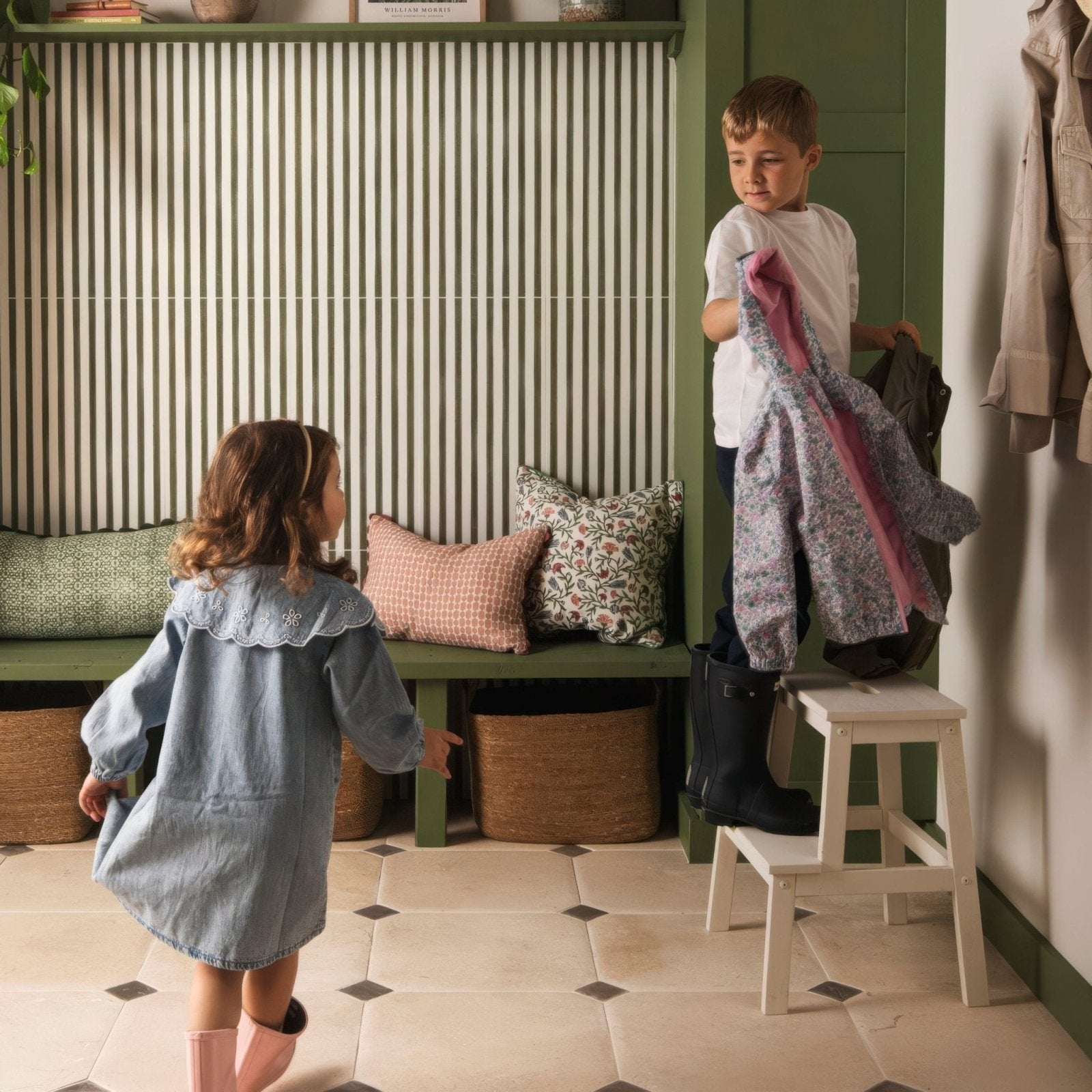 A child in a light blue denim dress with lace collar and pink boots stands near a green bench with patterned pillows in promenade hastings 60x30cm