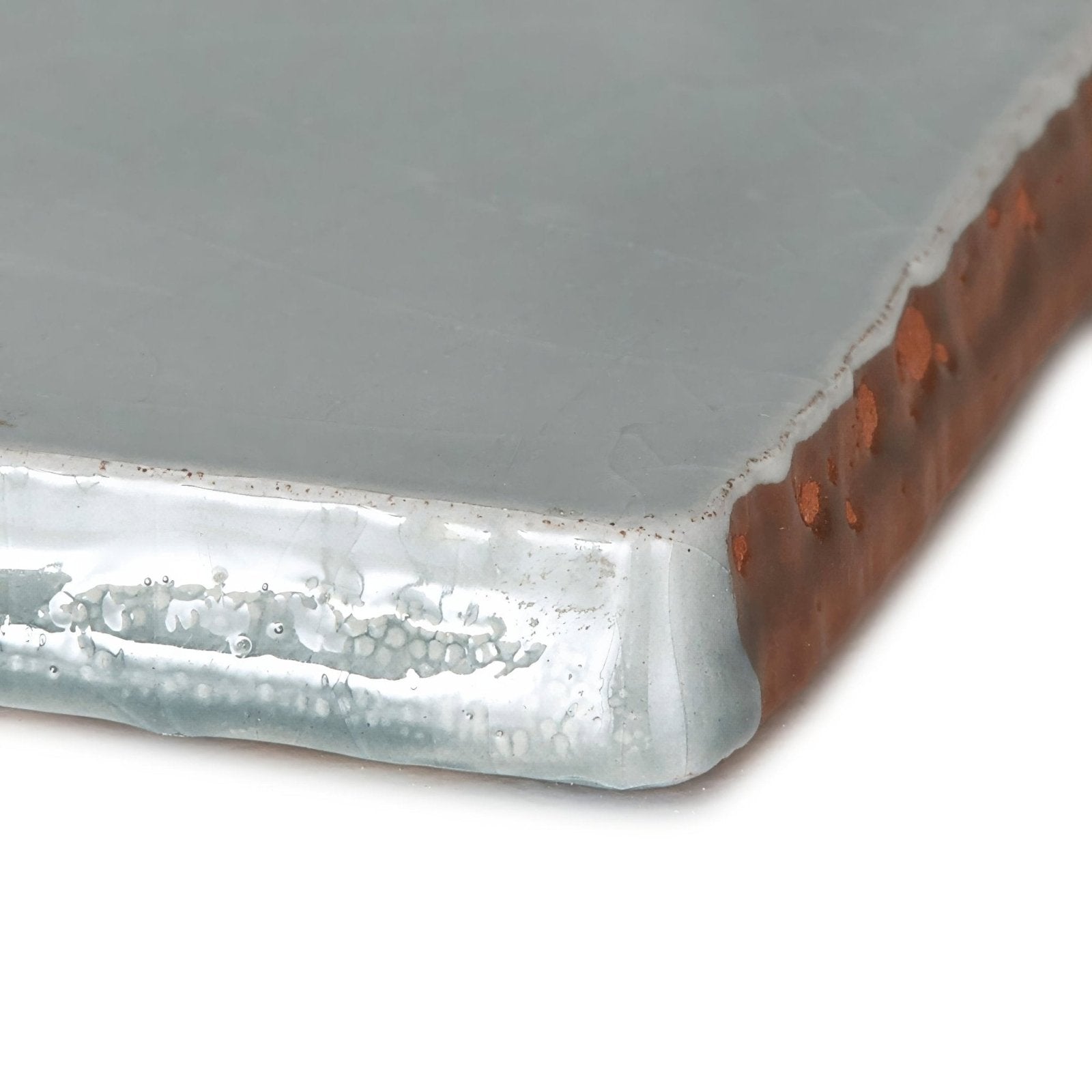 A provence falicon rectangle glass tile with frosted gray surface and rustic copper toned patina edges