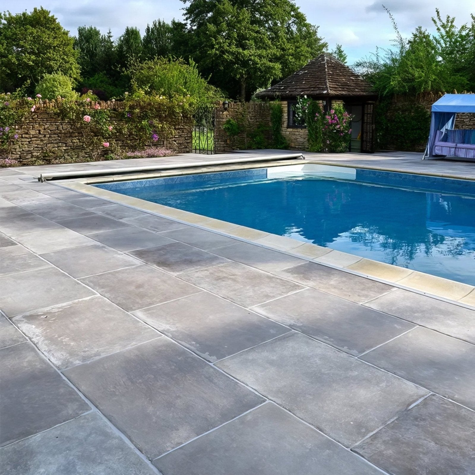Gray stone porcelain paving tiles in cenere color surrounding a blue swimming pool for outdoor patio use