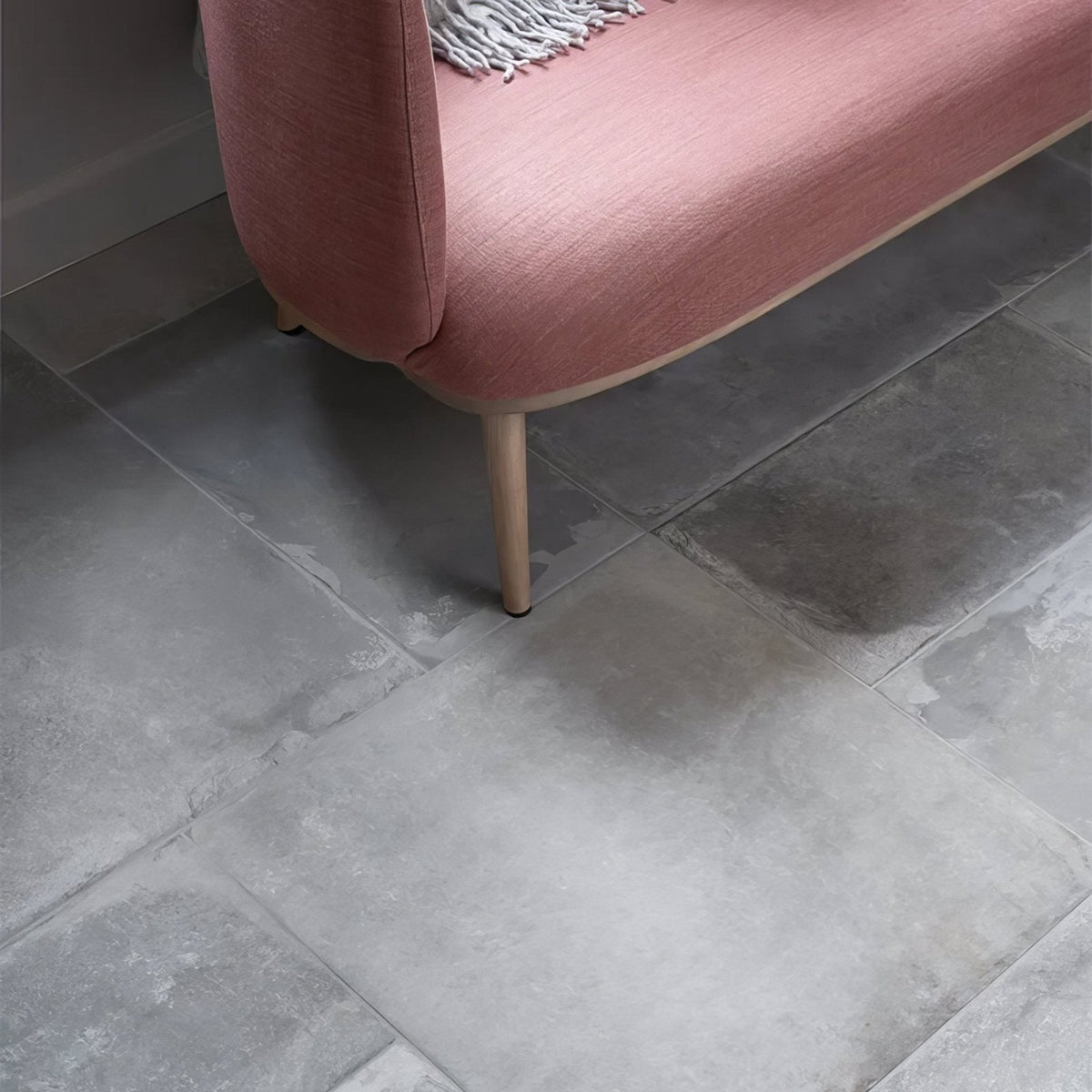 A soft pink upholstered Provence Porcelain Cenere bench with wooden legs and textured fabric surface