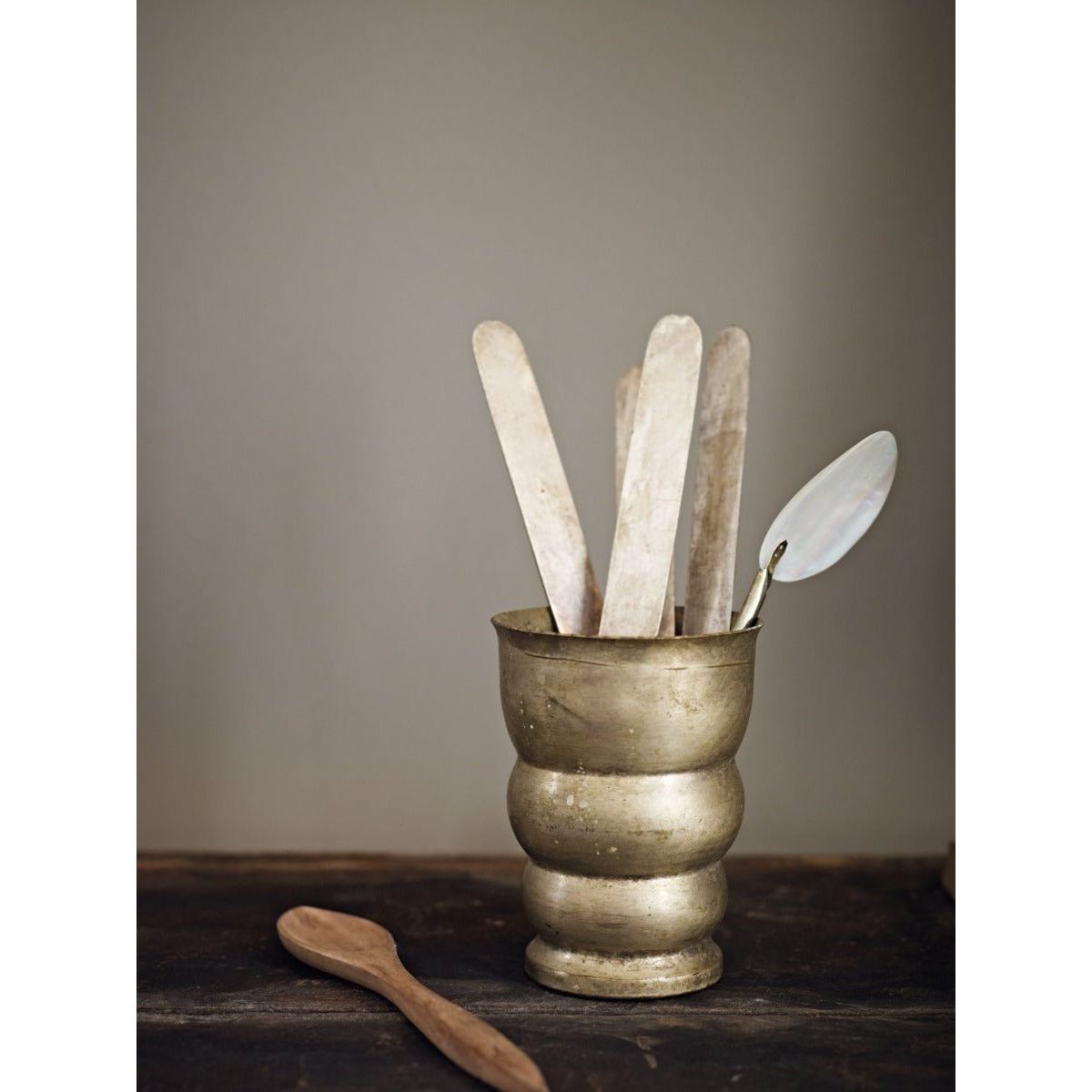 Antique brass-toned ceramic Pumblechook utensil holder with rounded body holding white wooden spatulas and a silver spoon