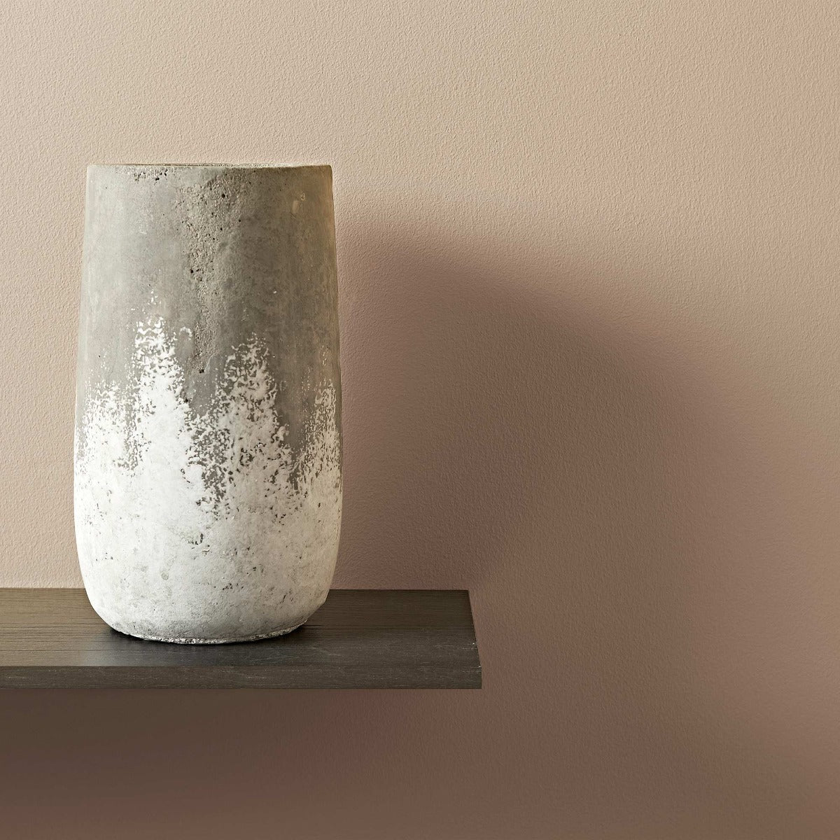 A pumice concrete vase with a textured matte finish and a subtle gray to white gradient on an uneven surface