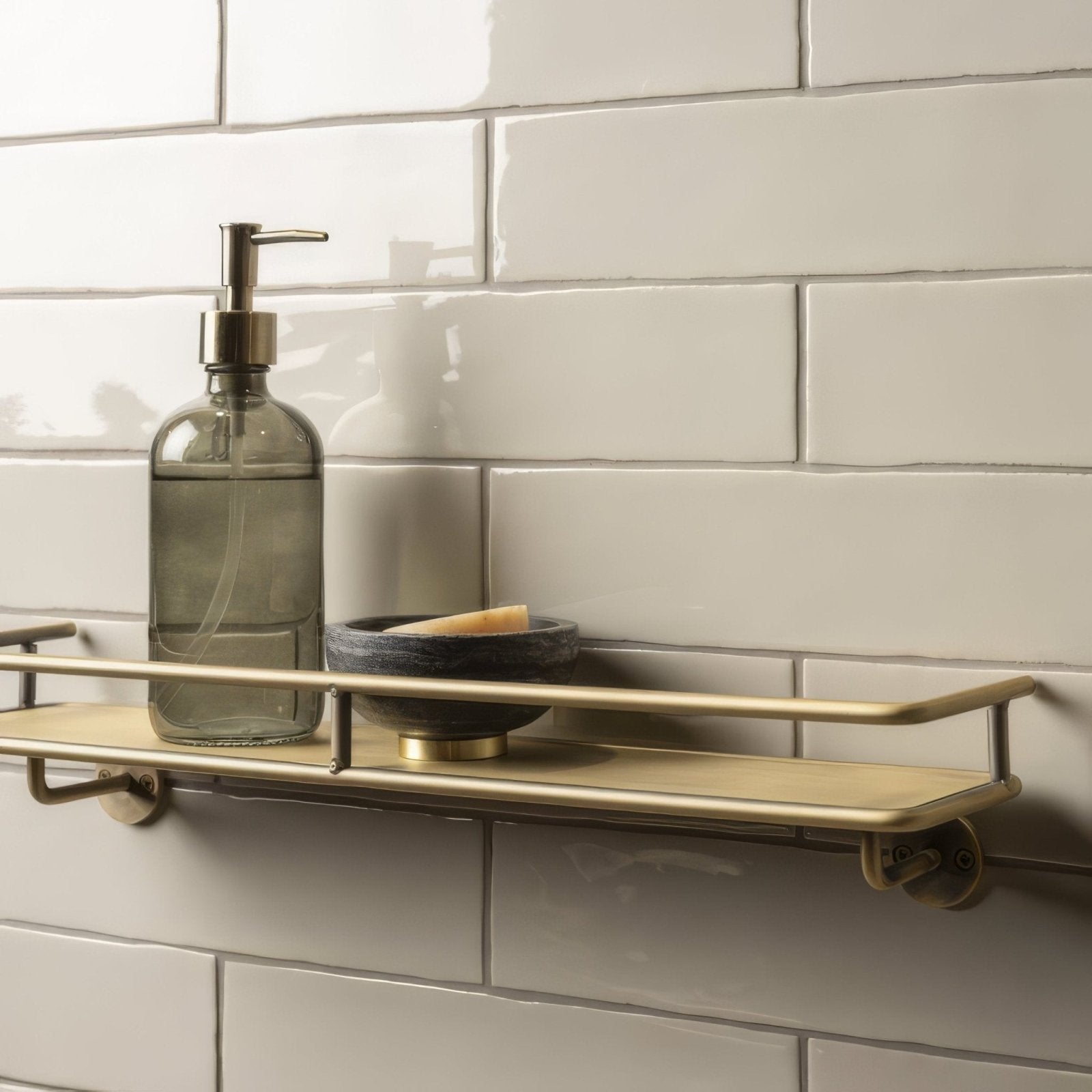 A sleek matte brass bathroom shelf with minimalist design holding a gray glass soap dispenser and black ceramic bowl