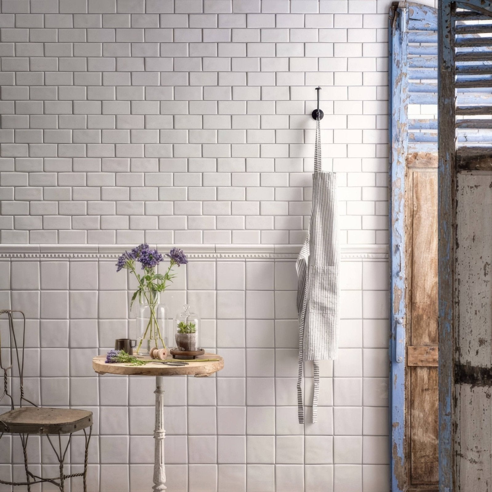 A black and white striped apron with a worn texture hanging on a hook next to pure white half tile walls