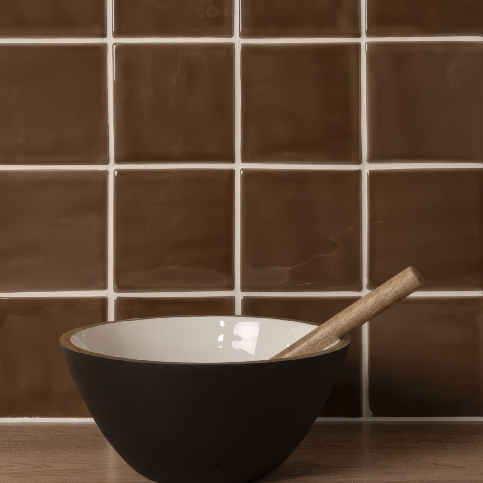 Black ceramic bowl with white interior and wooden spoon resting inside shown with putty field tile background