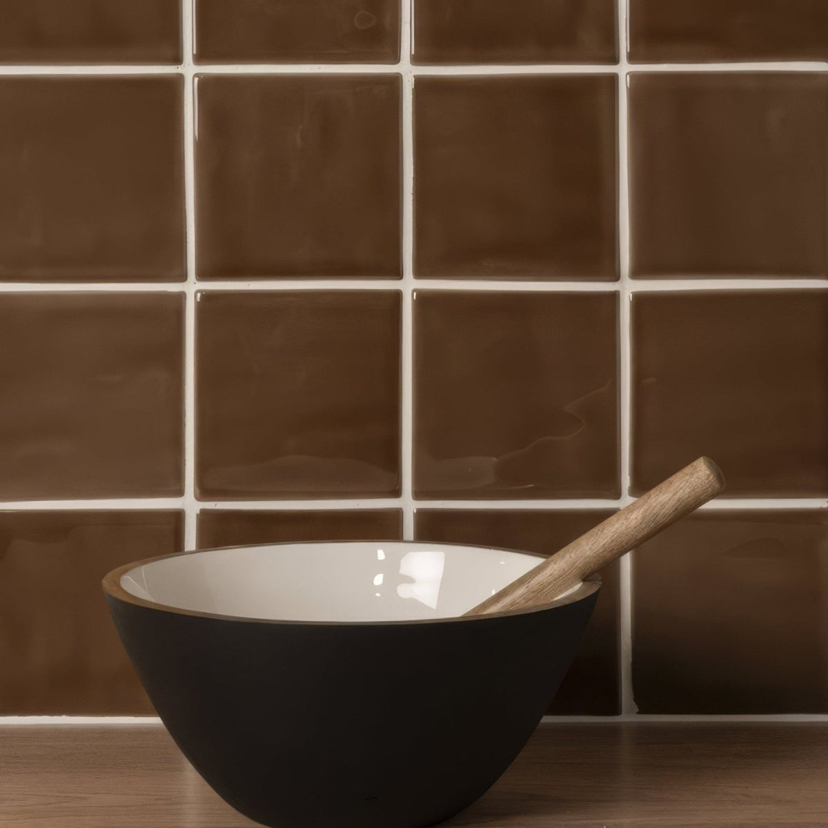 Black ceramic bowl with white interior and wooden spoon resting inside shown with putty field tile background