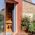 A cozy sunlit corner office featuring quarry red square terracotta-tiled walls with a wooden desk and stool