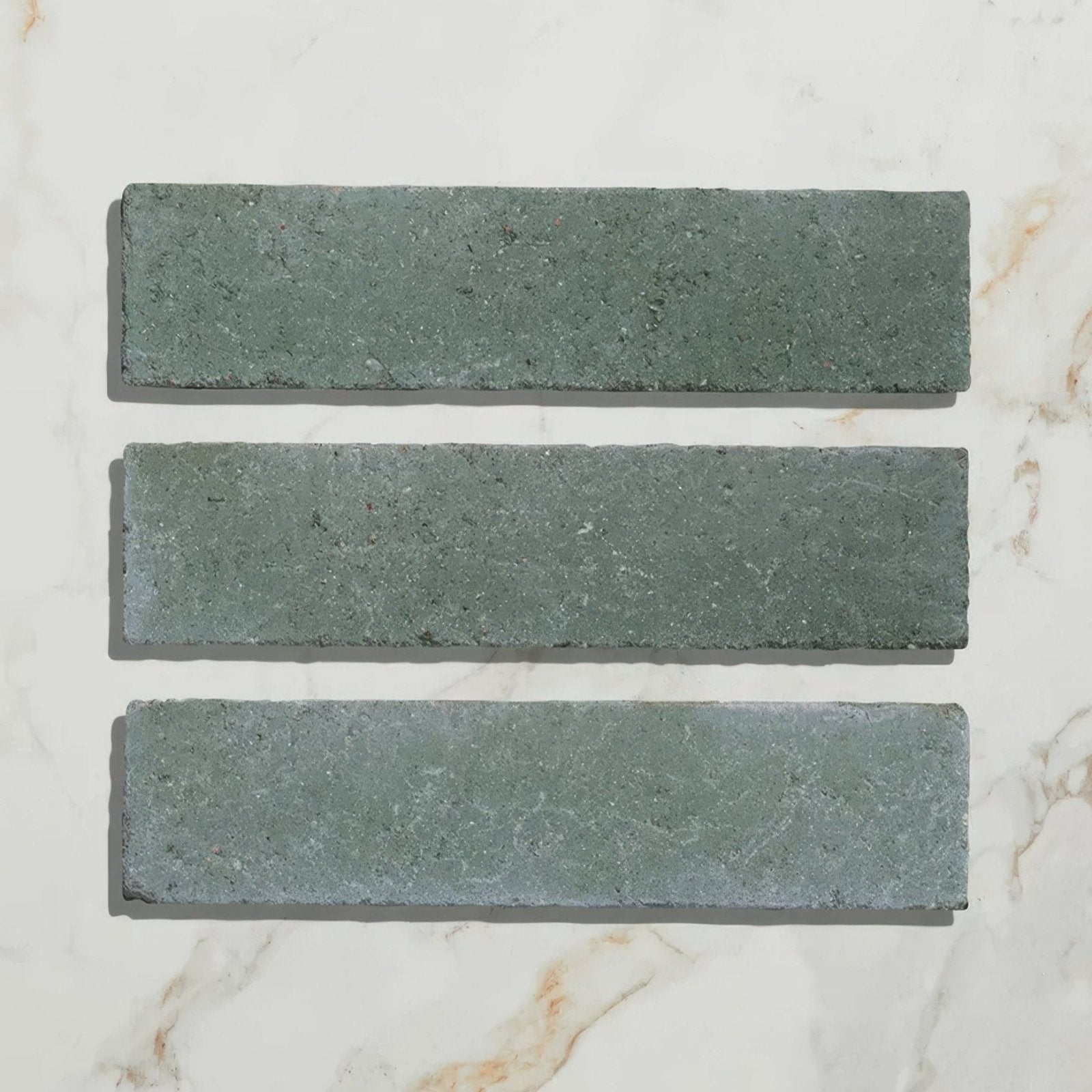 Three rectangular reform composite stone tiles with tumbled texture and muted leaf green color on natural slate surface