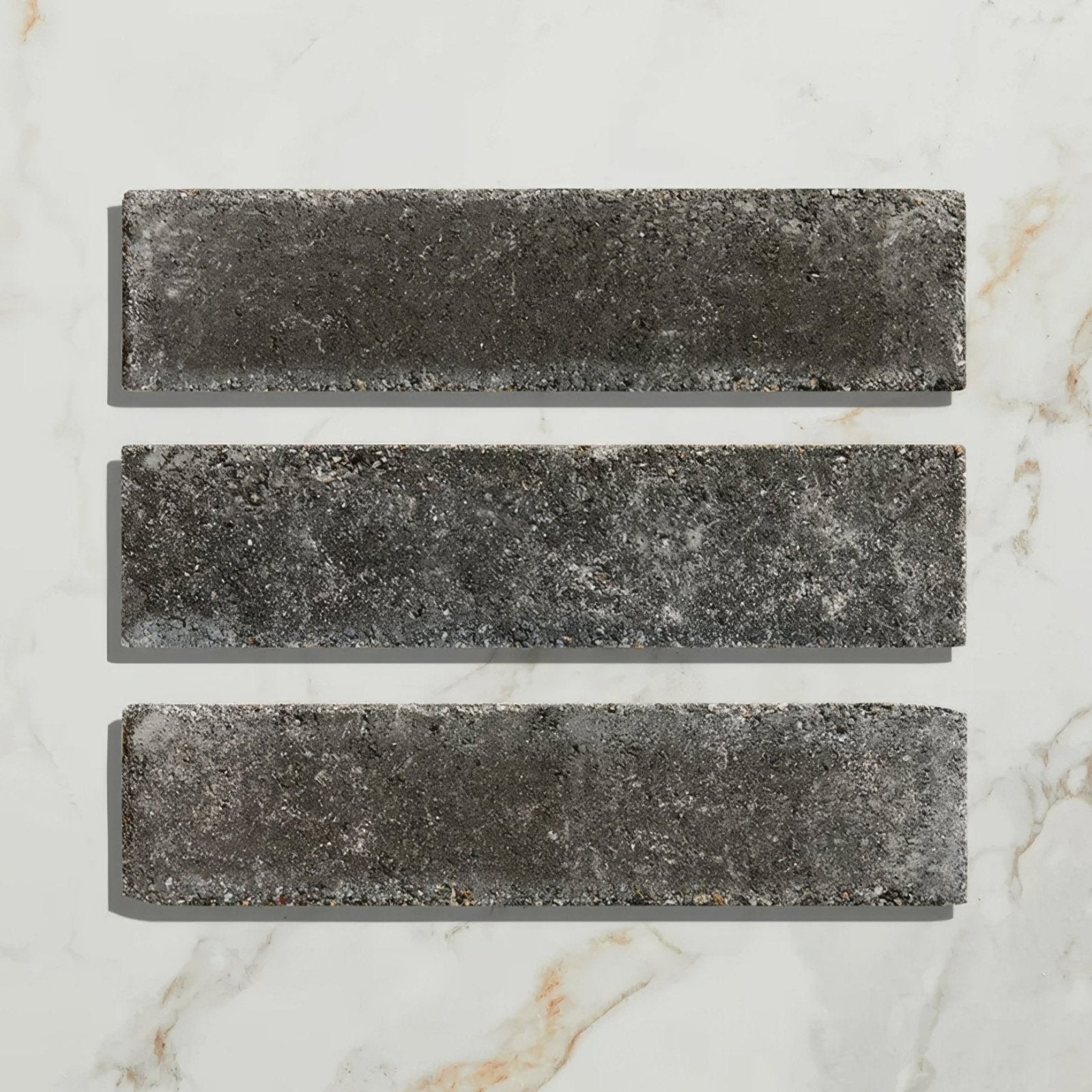Three dark gray textured reform composite stone tumbled nero rectangular tiles with a rustic weathered finish