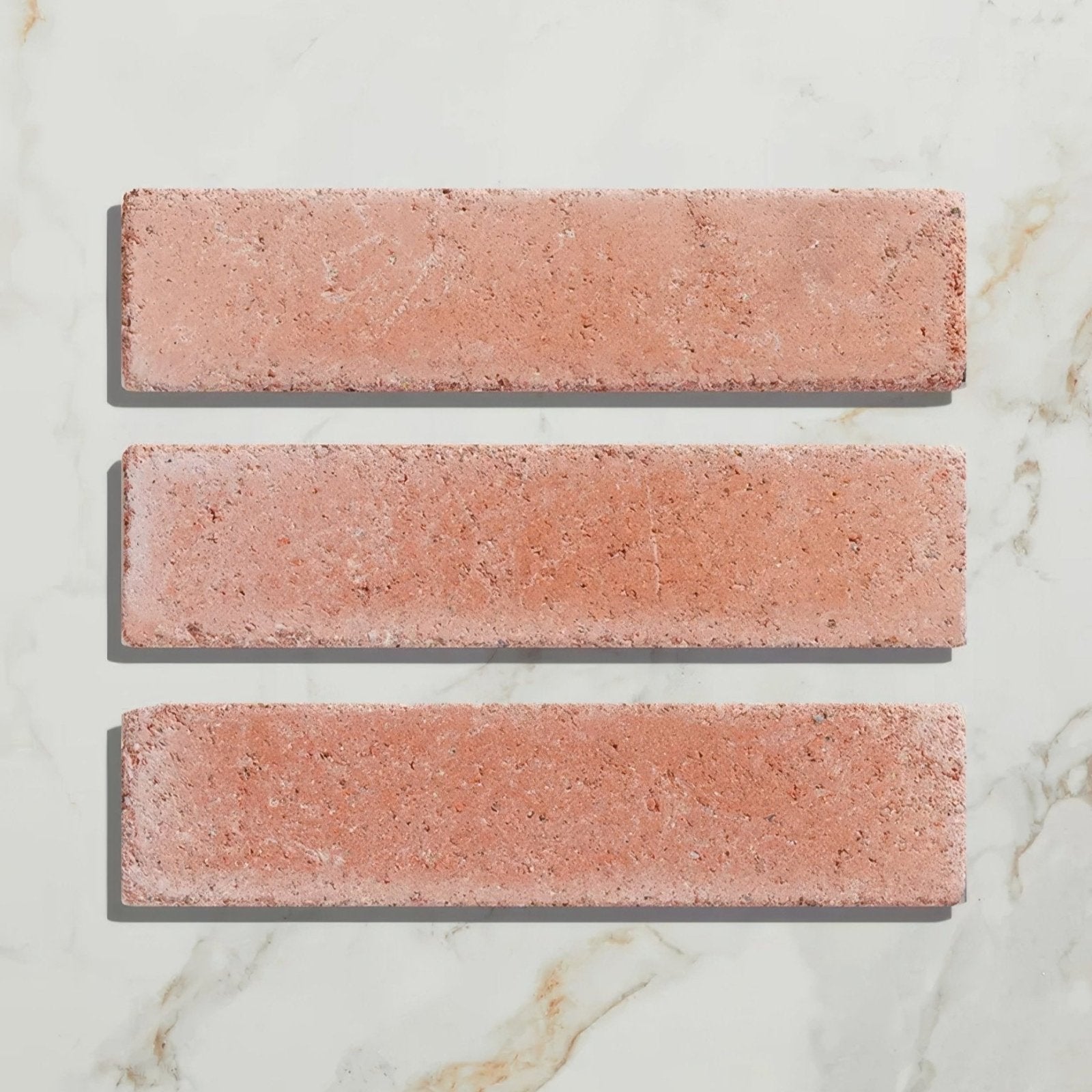 Three rectangular pink terracotta reform composite stone tumbled salmon pink tiles with a textured rustic surface