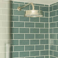 Shiny chrome showerhead with circular design and multiple nozzles paired with retro metro green park glazed tile