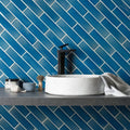 White marble vessel sink with a sleek black faucet against vibrant blue rockpool brick tile backsplash