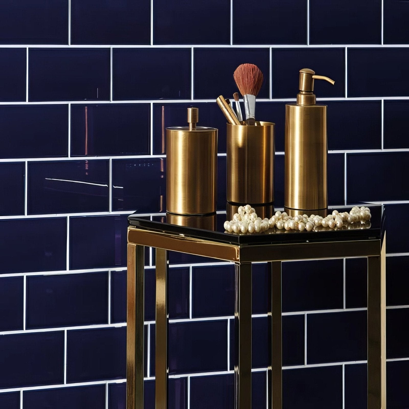Gold-toned bathroom accessory set with soap dispenser brush holder and container on royal blue half tile background