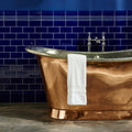 A polished copper freestanding bathtub with chrome fixtures and classic curved design from royal blue omega moulding