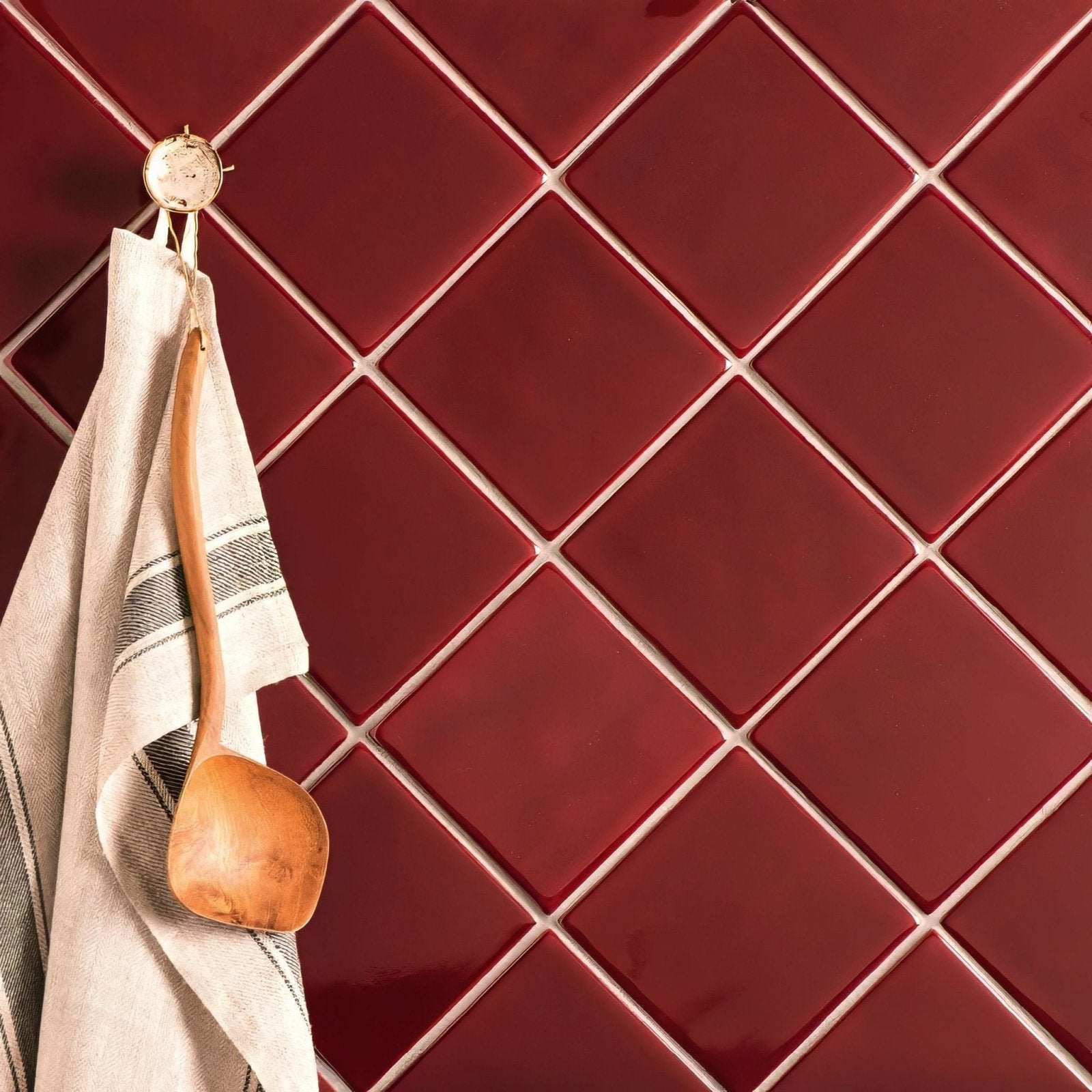 A wooden spoon with a smooth light brown finish hangs on a hook beside a striped towel against ruby field tile