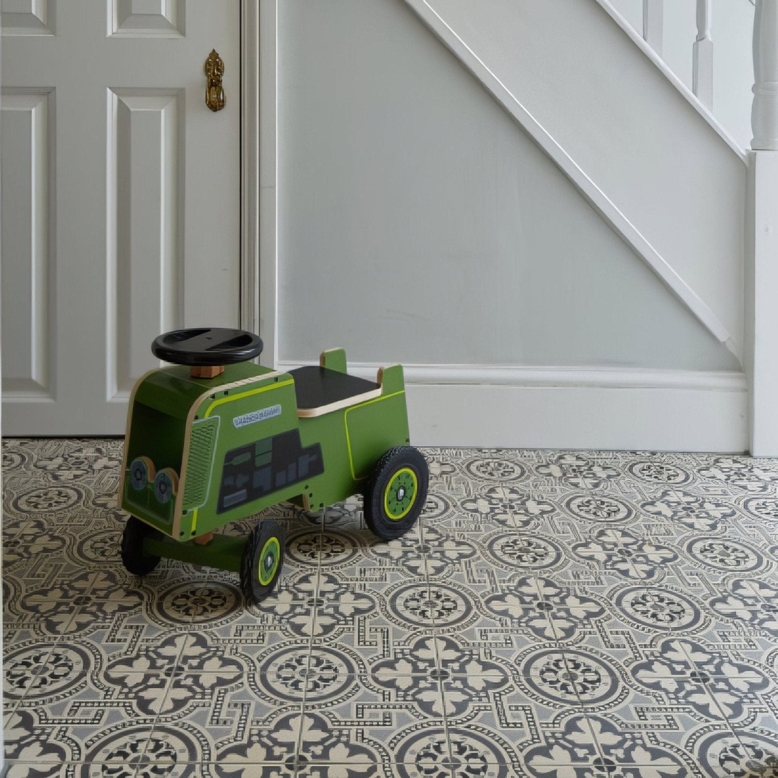 Green wooden toy tractor with black steering wheel and wheels featuring simple printed details on its side in Salisbury Black on Dover White