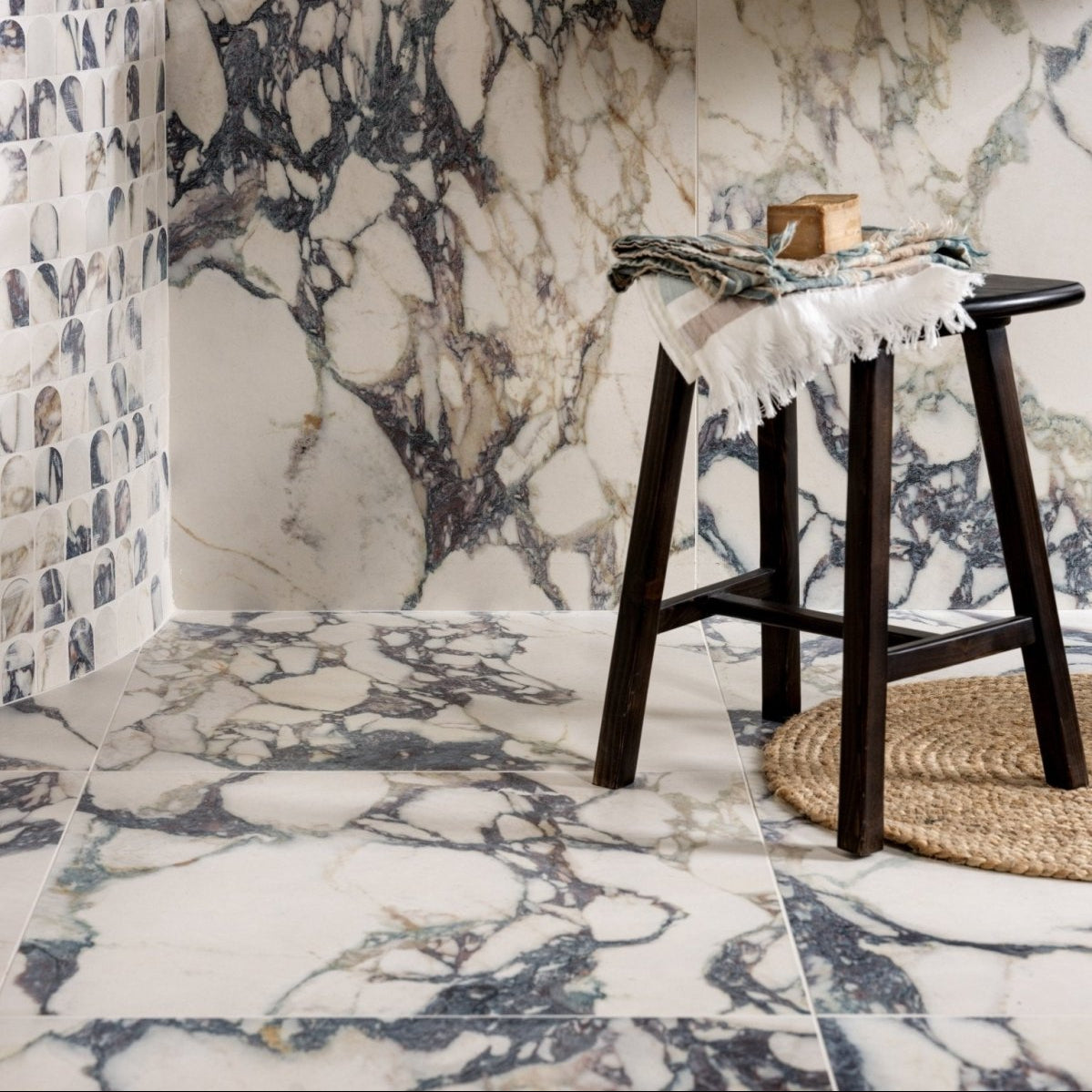 Dark wood stool with black seat and fringed white cloth paired with savoy novo porcelain matt arch mosaic tile panel