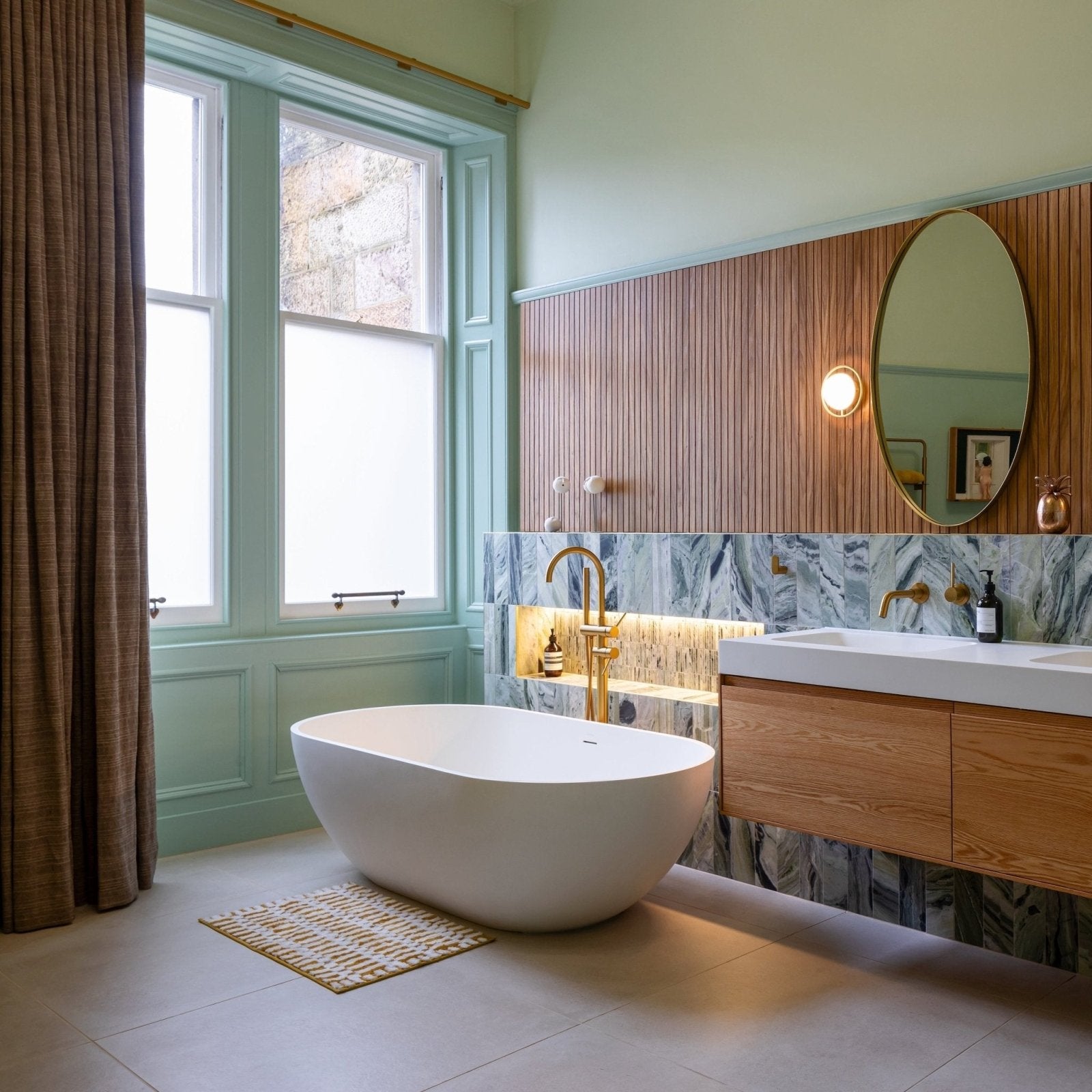 White freestanding bathtub with smooth rounded contours next to seaspray green marble tile 10 x 30cm wall