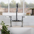 Chrome-finished bridge-style kitchen faucet with white ceramic handles shown with shell smooth brick tile background