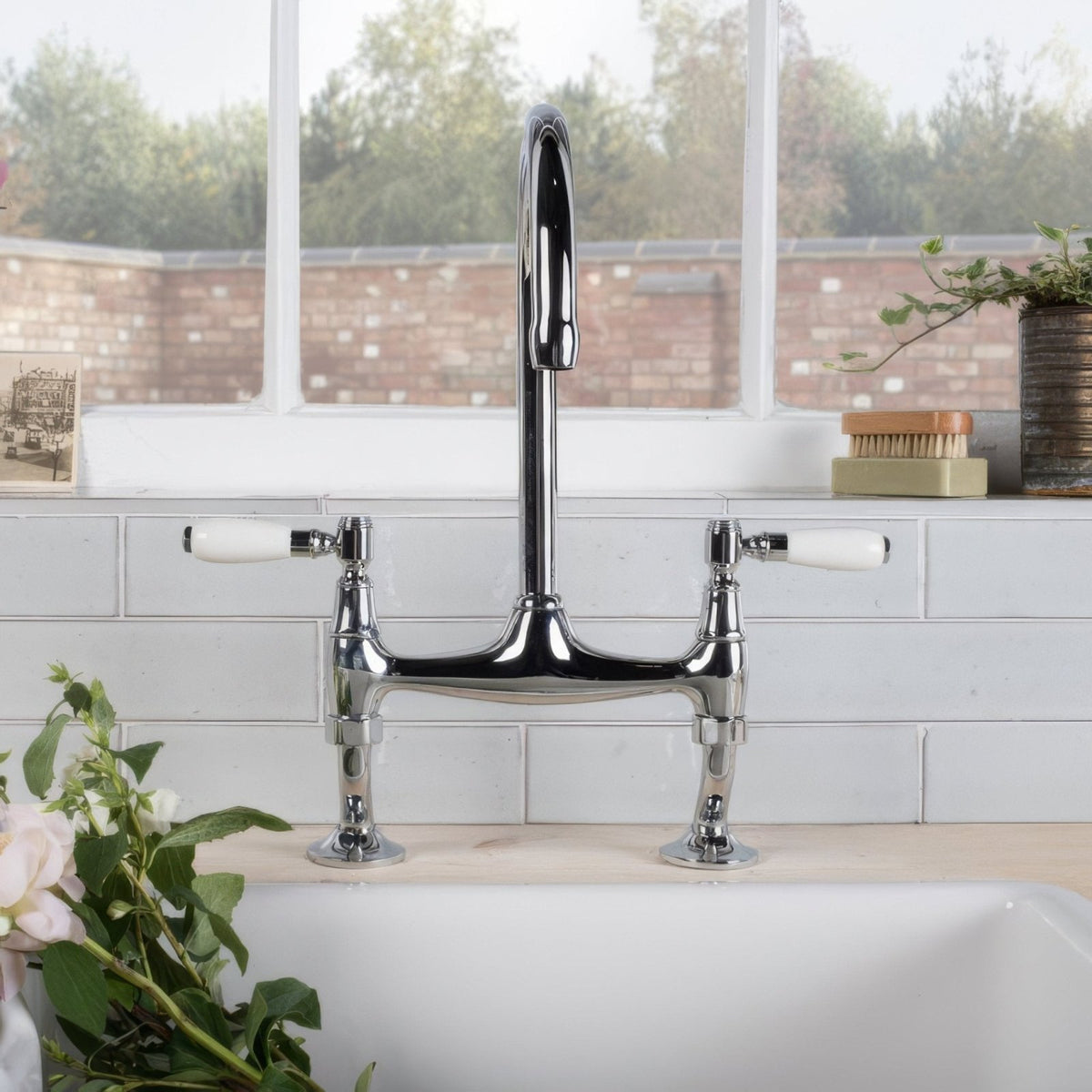 Chrome-finished bridge-style kitchen faucet with white ceramic handles shown with shell smooth brick tile background