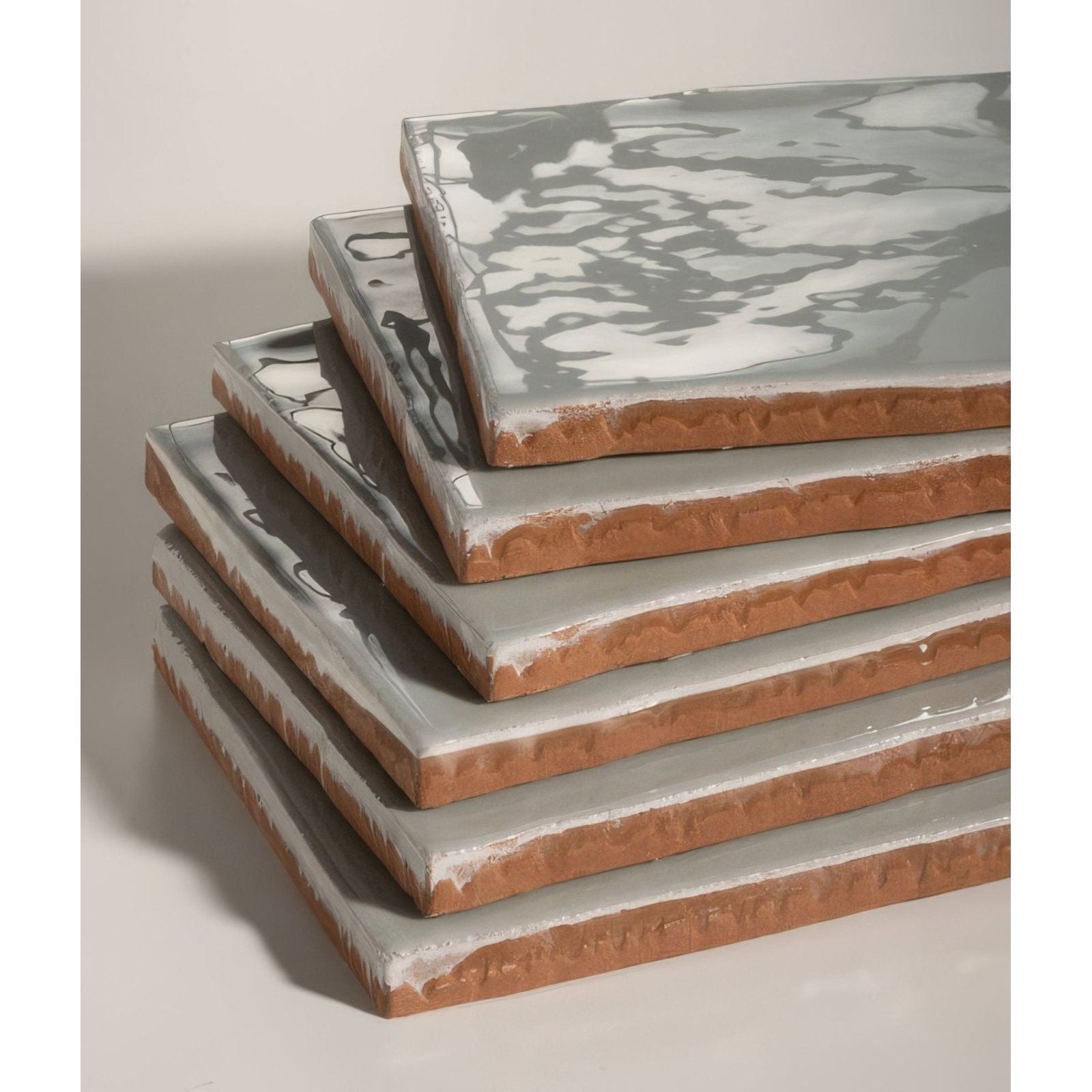 Stack of shoreline ceramic shingle tiles with gray and white marbled glaze and exposed terracotta edges