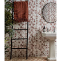 A rust-colored silk screen ceramic lantau bamboo chocolate towel with textured fringed edge hanging on a black ladder