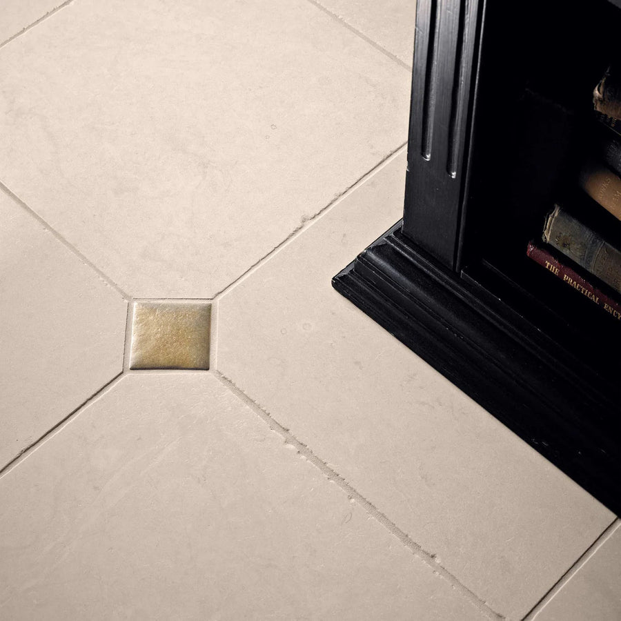 A small foundry cabochon inset gold metallic accent tile with a subtle texture next to beige ceramic floor tiles