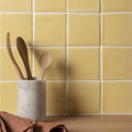Soft yellow field tile next to a white marble utensil holder with smooth surface holding wooden spoons and forks