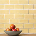 A light gray ceramic bowl filled with red and yellow apples on a wooden surface beside soft yellow half tile