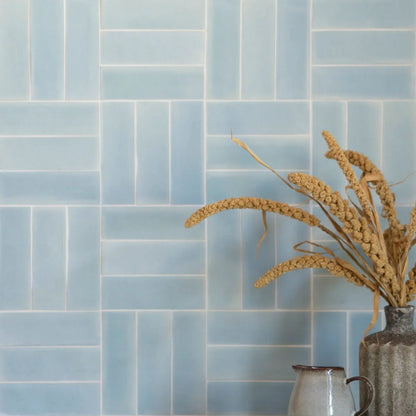 A rustic textured ceramic vase holding dried golden wheat stalks next to south cliff celeste brick tile