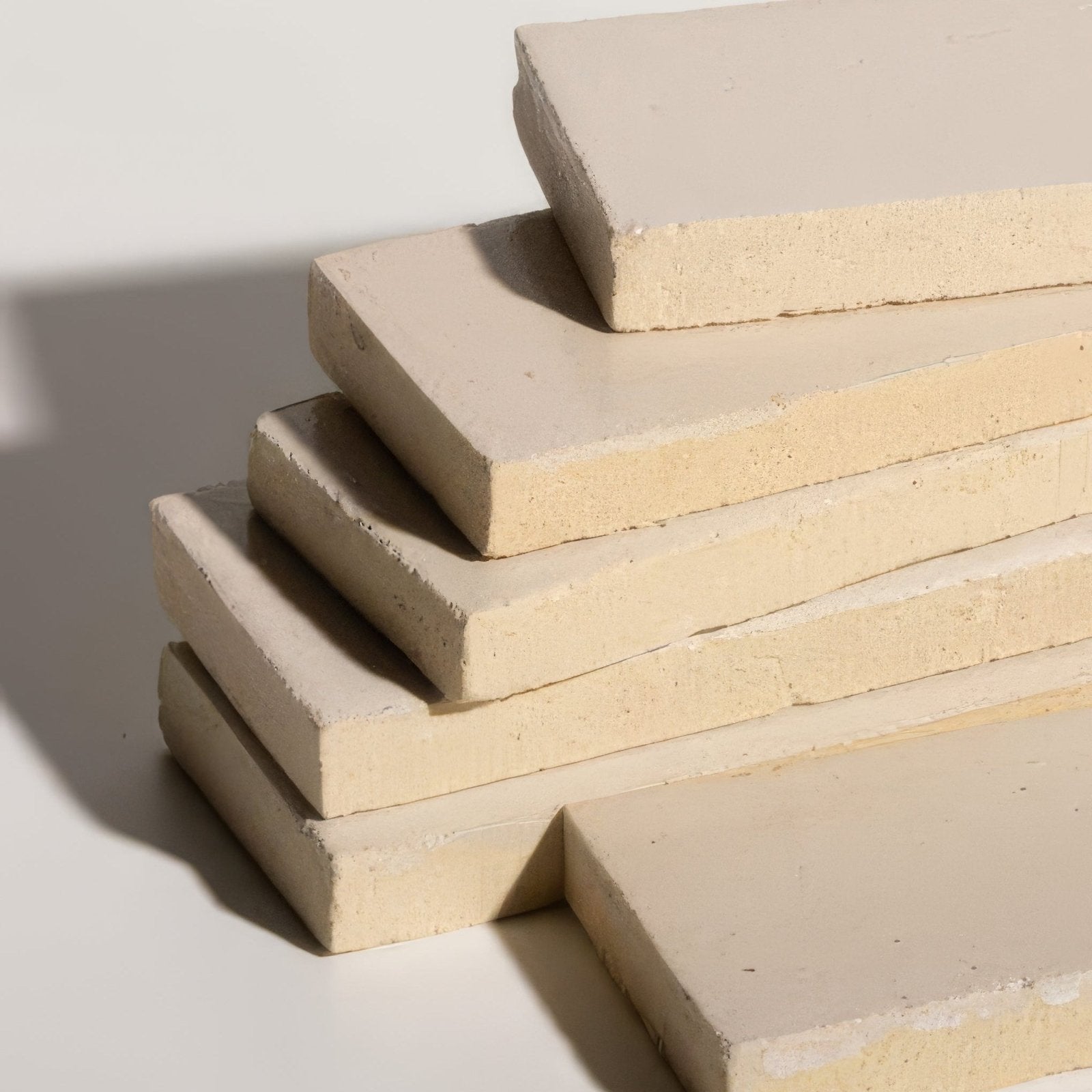 Stack of beige stone glaze ceramic chalkstone gloss brick slabs with textured edges and smooth matte surfaces
