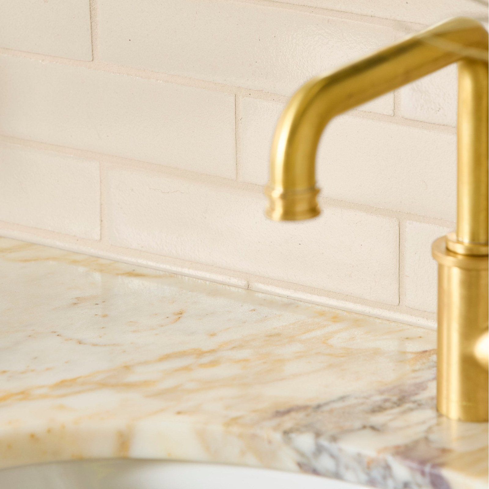Gold-toned faucet with sleek curved spout and cylindrical base paired with stone glaze ceramic linen gloss brick