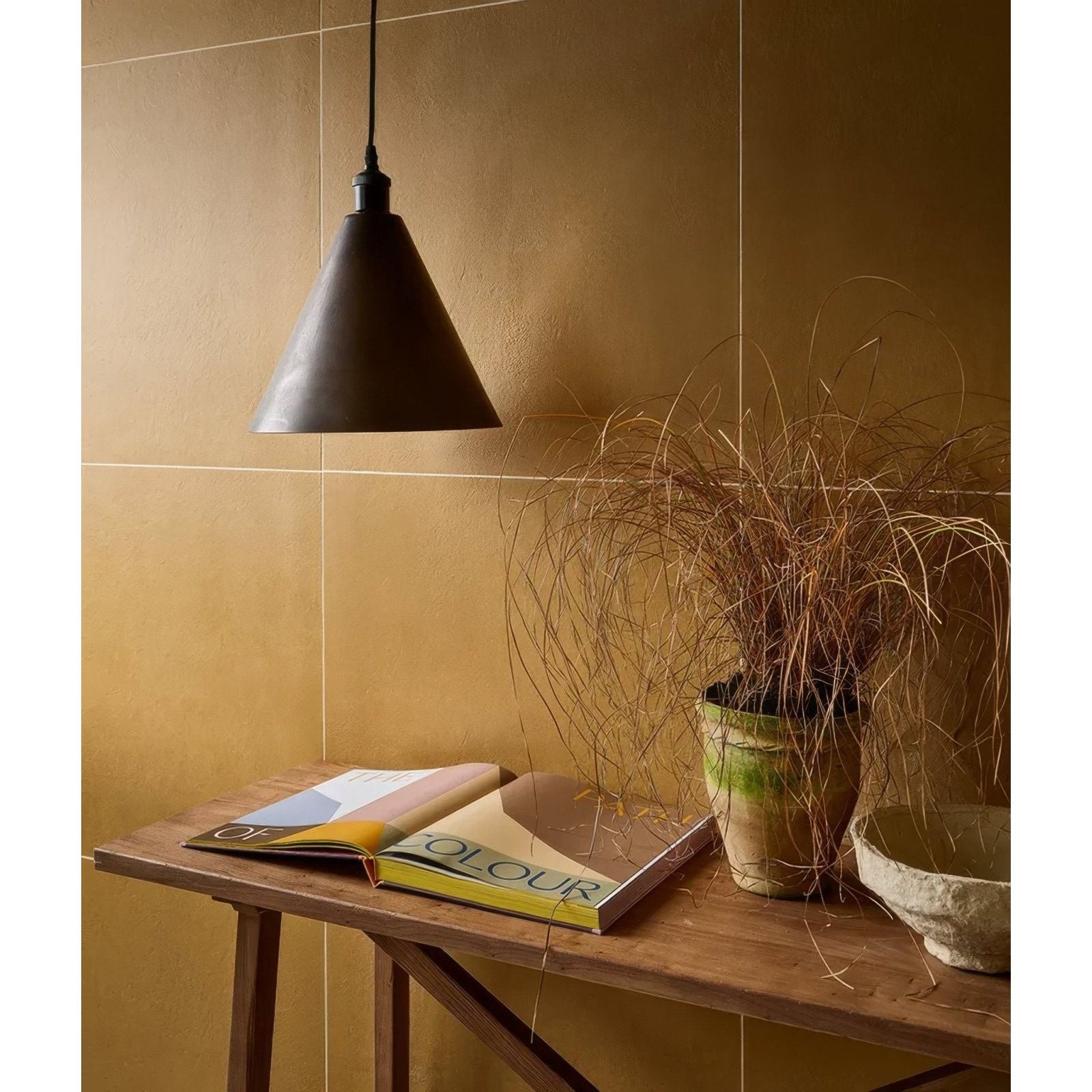 Dark matte-finished metal pendant lamp with conical shade hanging from black cord in stucco porcelain textured mustard