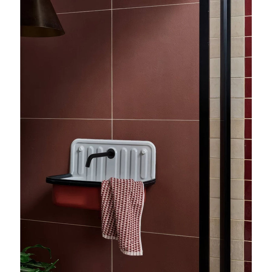 White enamel wall-mounted stucco porcelain textured red sink with black faucet and vertical ridges on back panel