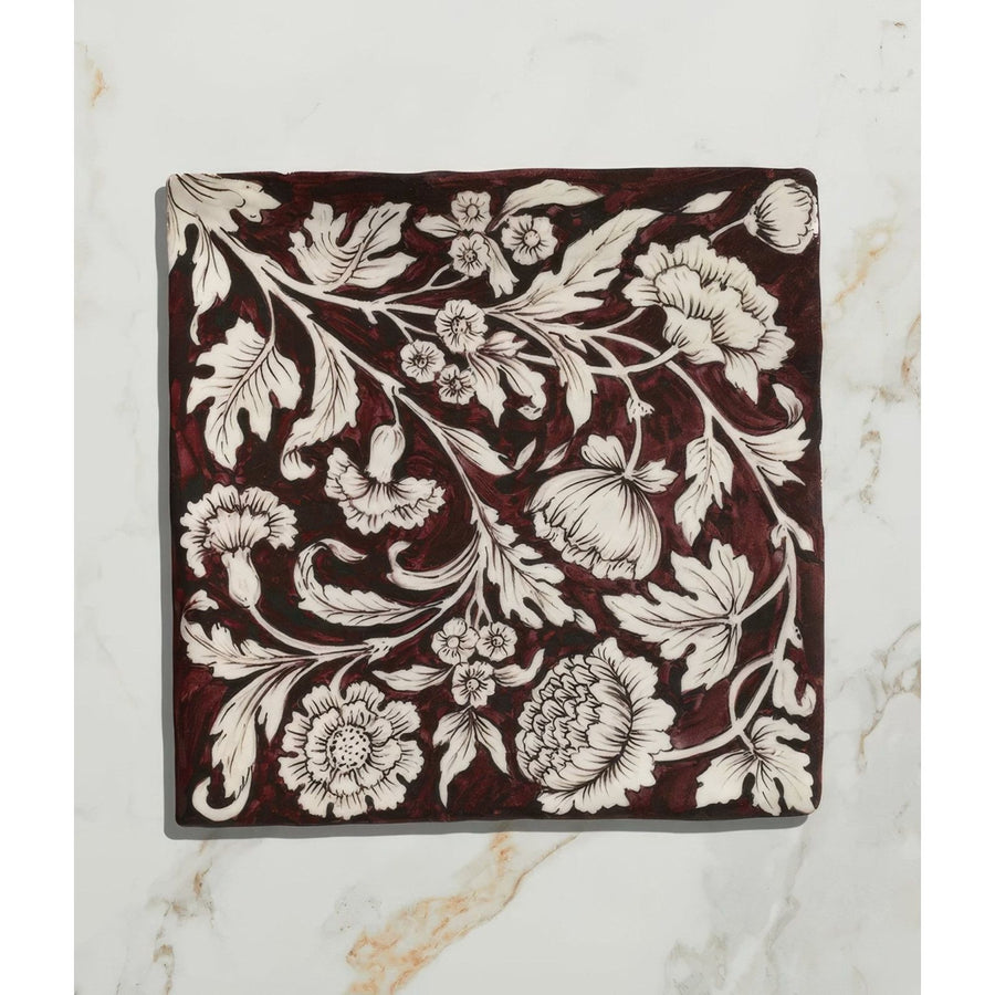 Studio Assisi Red ceramic square tile with deep burgundy glaze and intricate white floral pattern of leaves and vines
