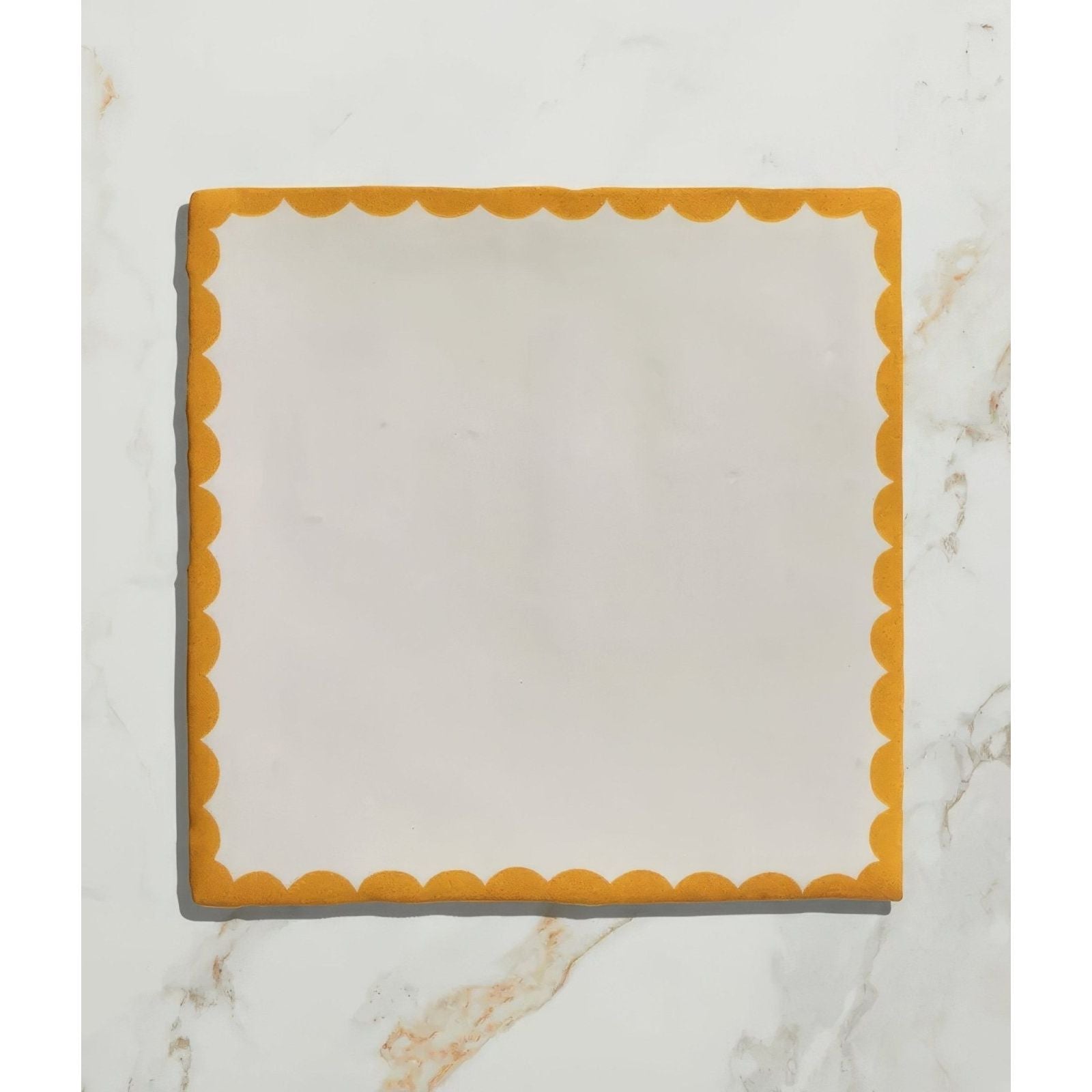 A square ceramic plate by studio bobbin with a scalloped mustard yellow rim and smooth off white center
