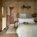 A woven wicker basket filled with bread resting on a bed next to studio cosmos midnight ceramic items