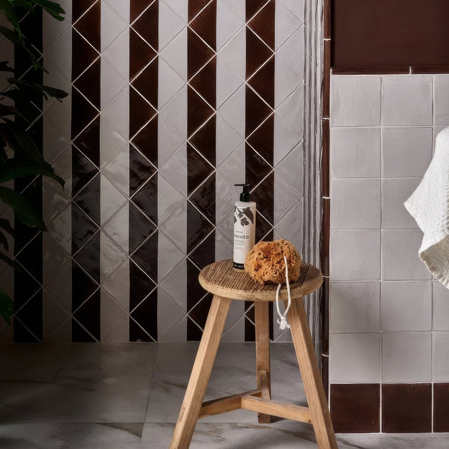 White ceramic pump bottle with black leaf design labeled dashed on wooden stool beside orange loofah in Studio Jamboree collection