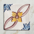 Studio Nonna’s Kitchen Cornelia ceramic tile features a hand-painted yellow flower with blue and mauve accents on off-white