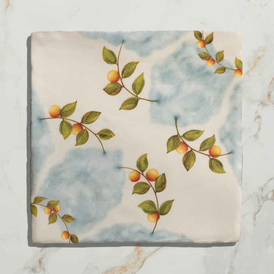 A ceramic tile from studio nonnas kitchen nuvola arancio with hand-painted green leaves and orange fruits design