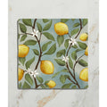 Square ceramic coaster from Studio Nonna’s Kitchen featuring yellow lemons green leaves and white blossoms on soft blue background