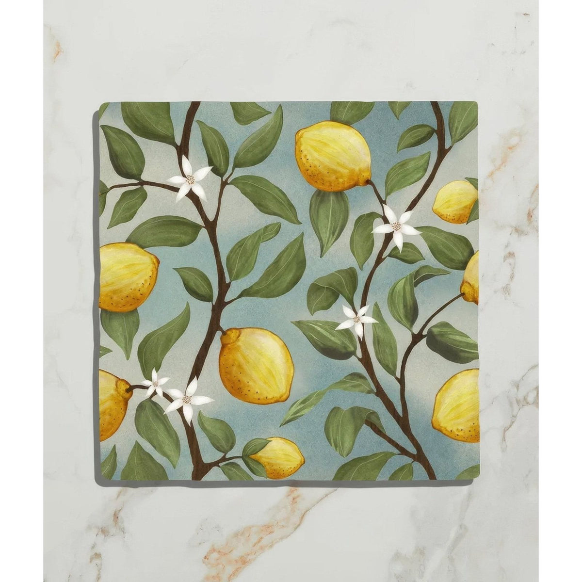 Square ceramic coaster from Studio Nonna’s Kitchen featuring yellow lemons green leaves and white blossoms on soft blue background
