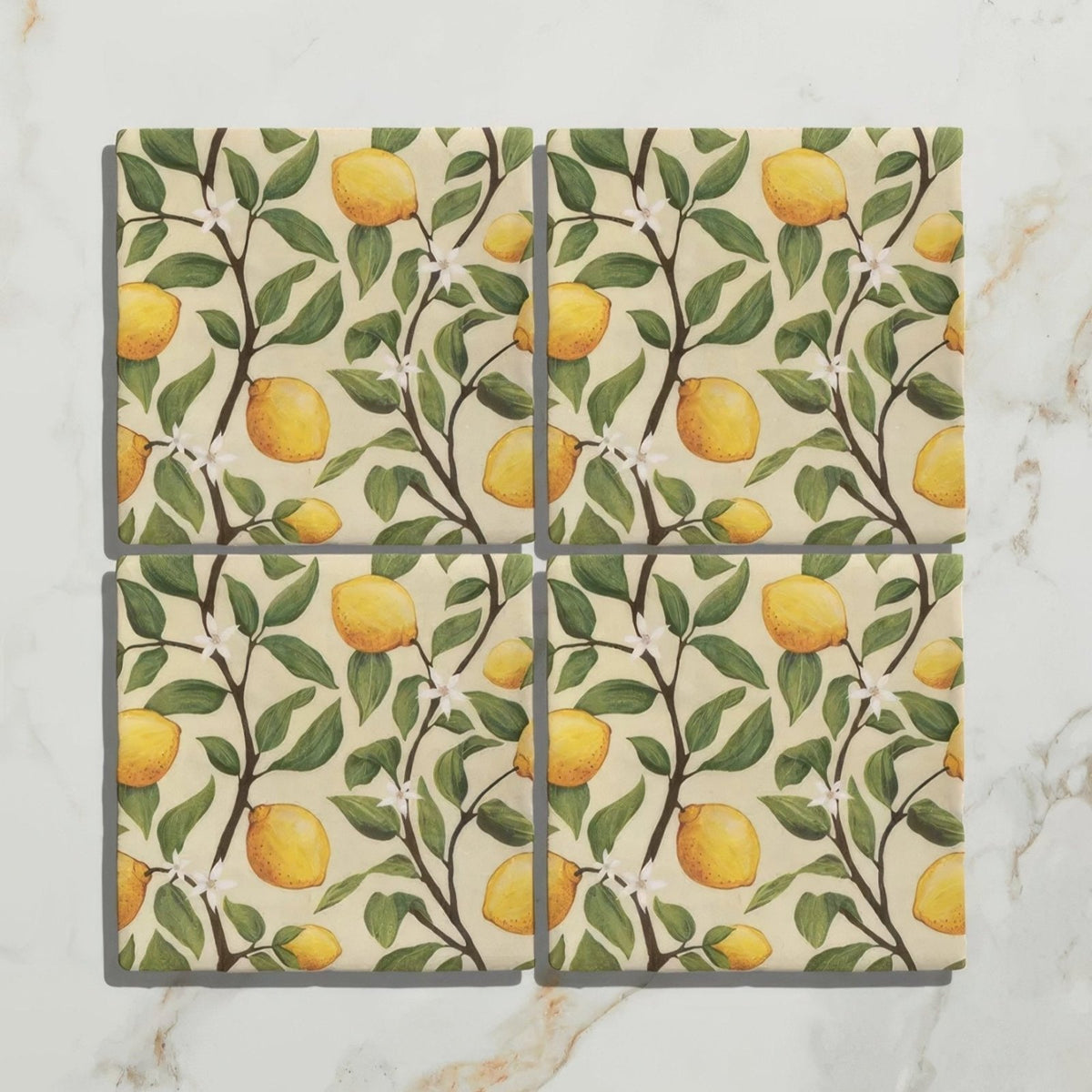 Set of four Studio Nonna kitchen Sorrento Sabbia ceramic coasters with yellow lemon and green leaf pattern on off-white background