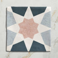 A square ceramic tile from Studio Souk featuring a geometric star pattern in navy gray and blush pink tones