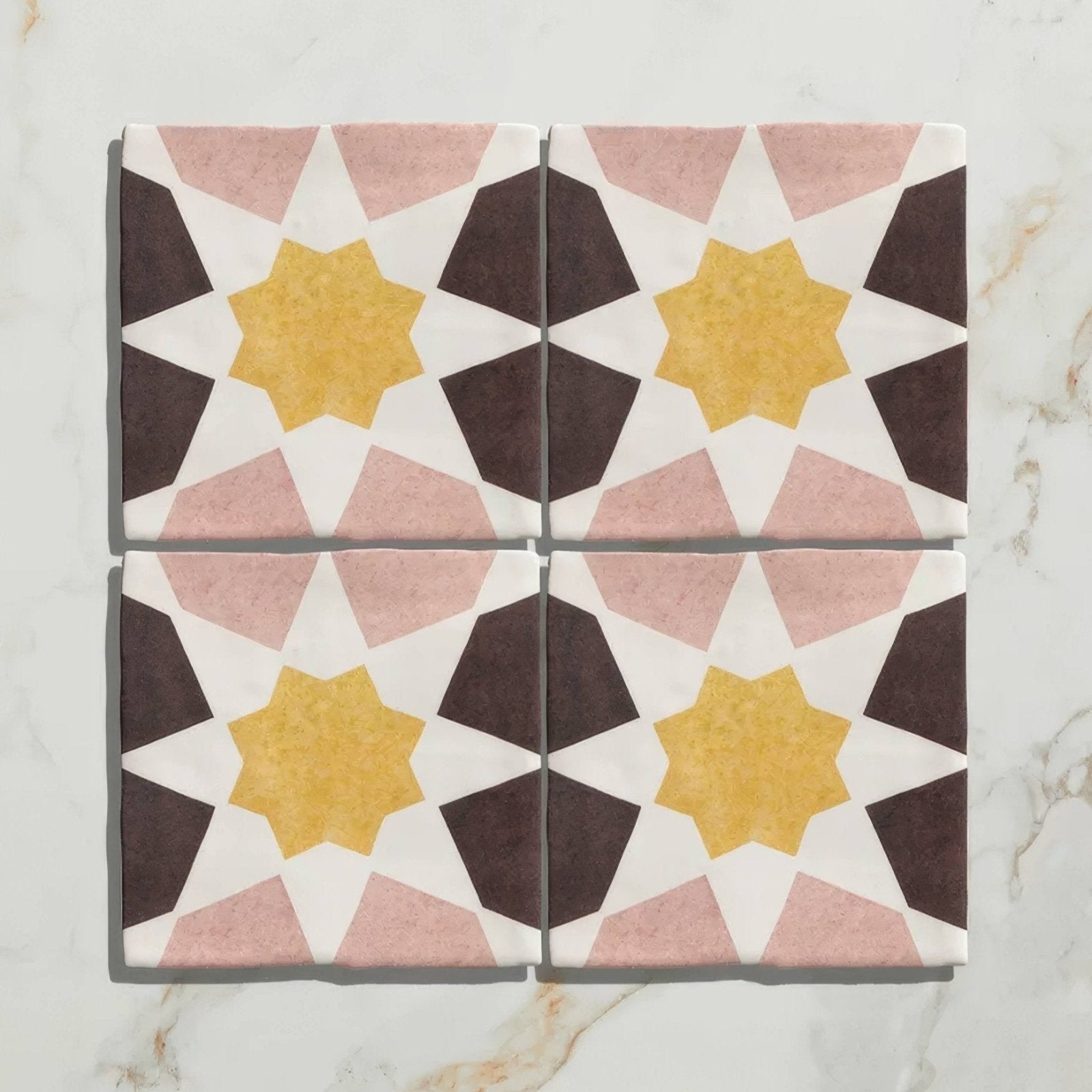 Four square ceramic tiles from Studio Souk featuring yellow star geometric patterns with pink and dark brown shapes on white