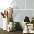 Cream-colored ceramic pitcher holding wooden spoons and metal whisk in Sudbury Field Tile setting